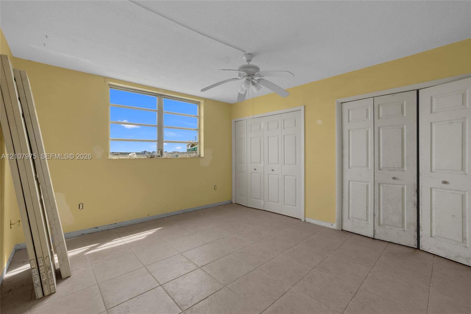 Interior space featuring tile flooring, dual bi-fold door closets, a multi-pane window, and a ceiling fan with integrated lighting