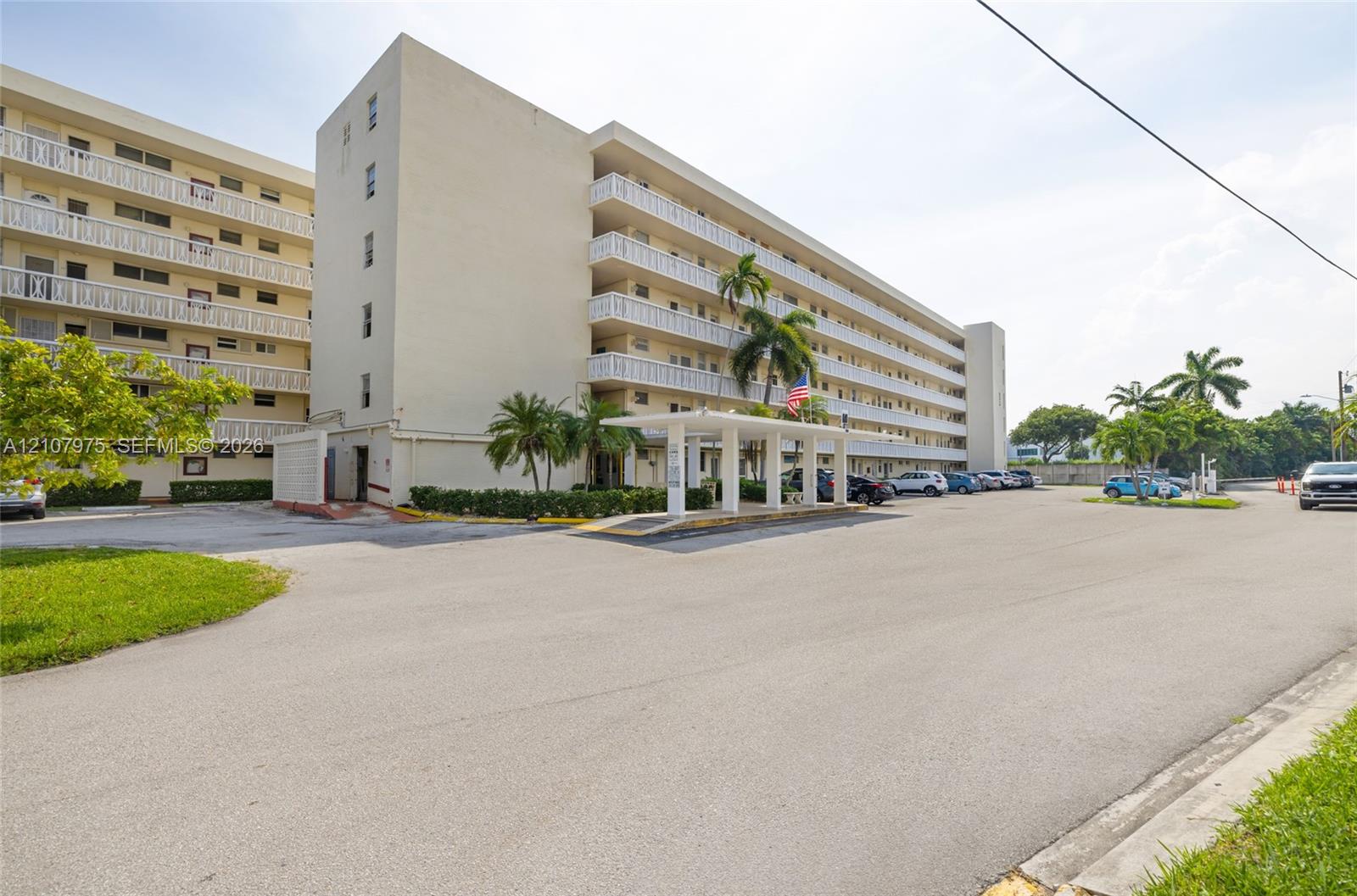 Multi-story exterior featuring a covered porte-cochre, balcony railings on each level, and integrated landscaping with mature palm trees
