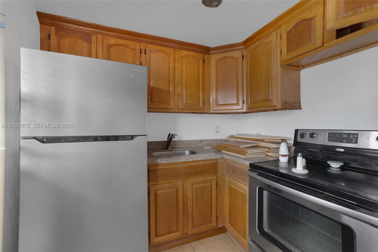 Kitchen featuring natural wood-finish cabinetry, speckled stone-composite countertops, stainless steel refrigerator, and a stainless steel electric range