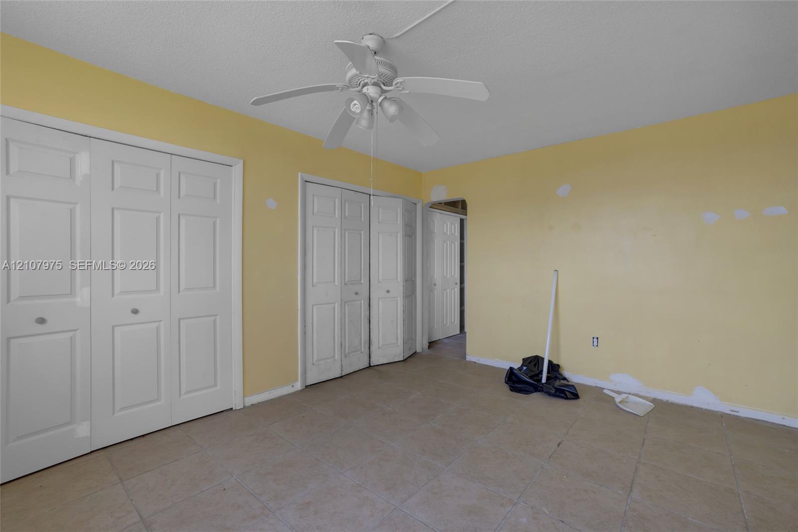 Room featuring ceramic tile flooring, a white ceiling fan with integrated lighting, and two sets of bi-fold closet doors
