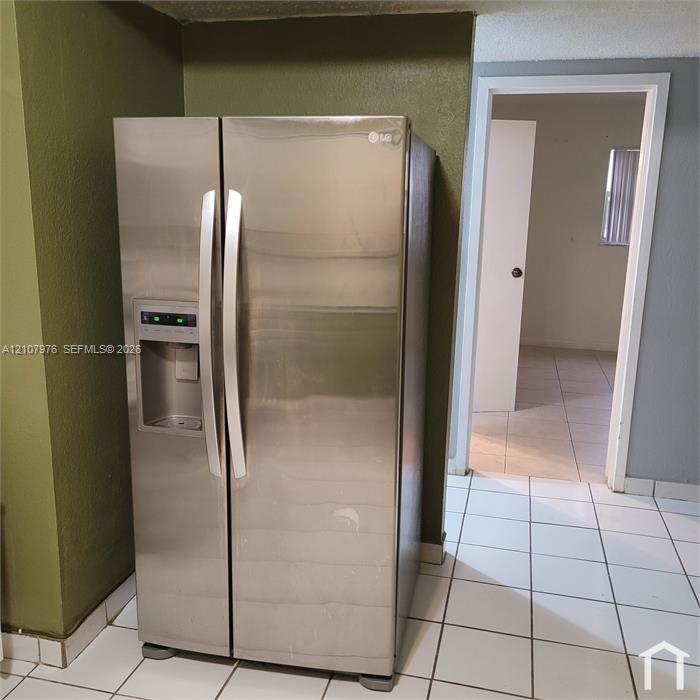 Stainless steel side-by-side refrigerator with external water and ice dispenser, white ceramic tile flooring, and solid-core interior doors