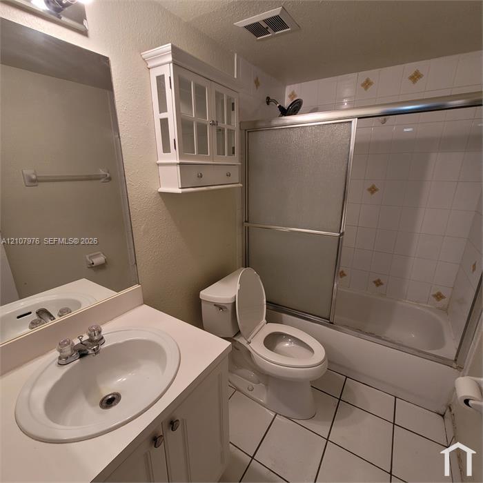 Bathroom featuring a vanity with an integrated basin, a wall-mounted glass-front cabinet, a shower-tub combination with sliding glass doors, and tiled flooring