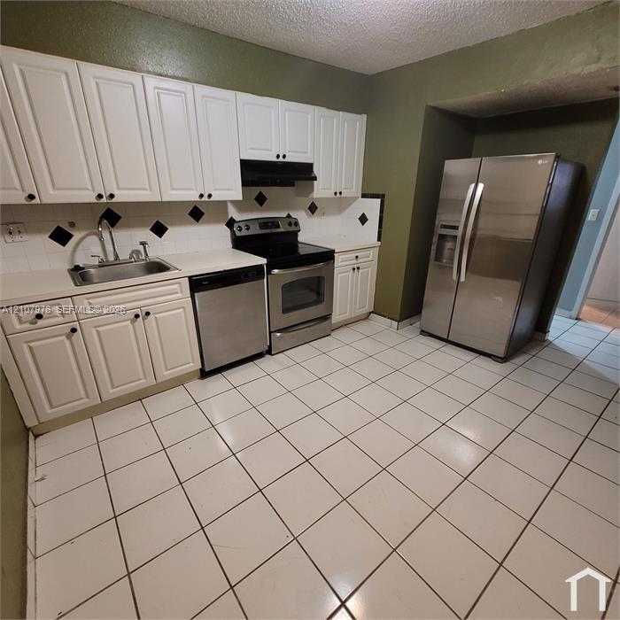 Kitchen featuring white shaker-style cabinetry, stainless steel appliances, ceramic tile flooring, and a decorative tile backsplash