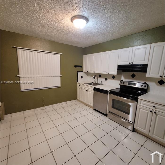 Kitchen featuring white cabinetry, stainless steel appliances, ceramic tile flooring, and a tiled backsplash with decorative accents