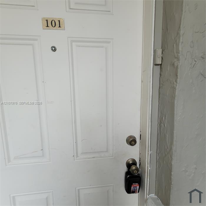 White six-panel entry door with brass-tone hardware, integrated peephole, and door-mounted identification plaque