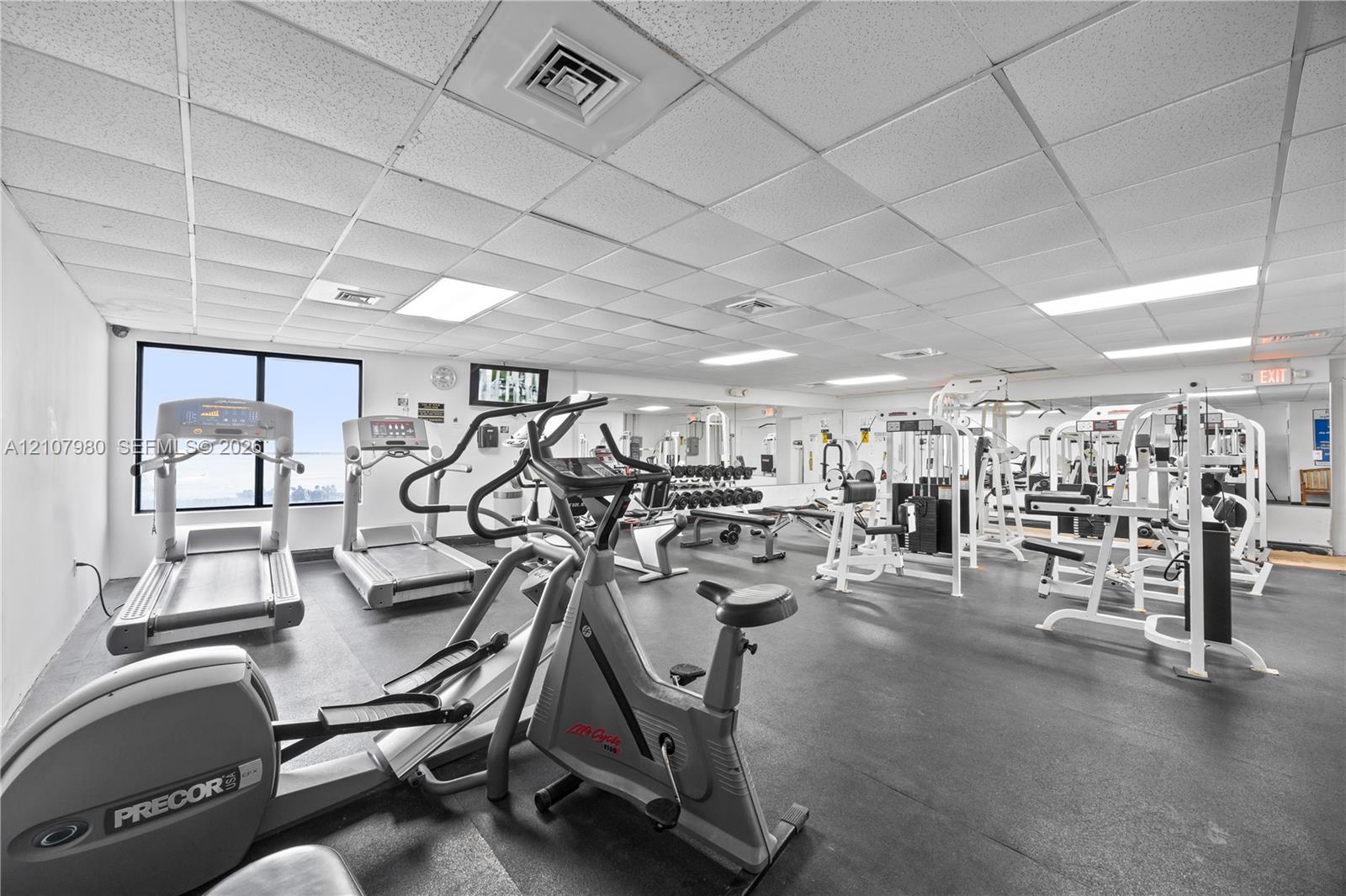 Fitness center featuring rubber flooring, drop ceiling with recessed lighting, and wall-to-wall mirrors
