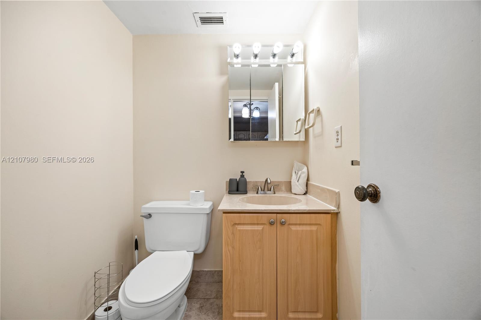Light-toned wood vanity with a solid-surface integrated sink, mirrored medicine cabinet with integrated lighting, and a neutral-toned toilet