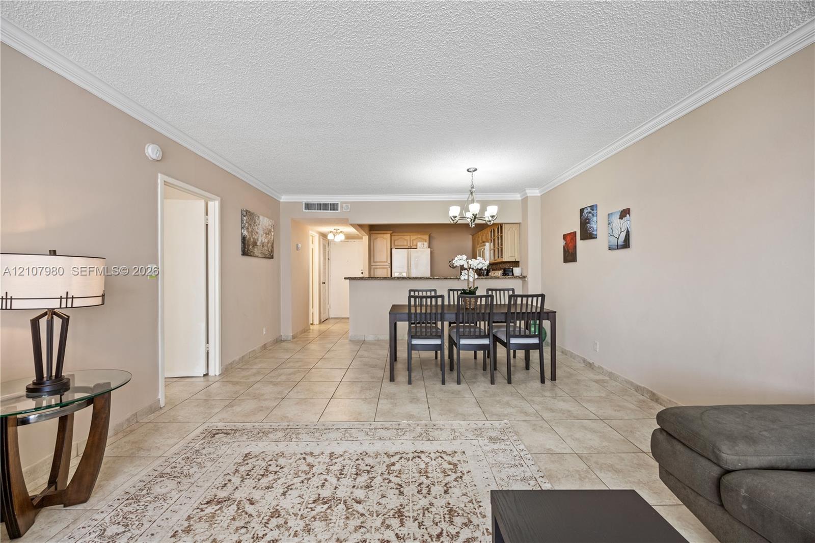 Open-concept living space featuring ceramic tile flooring, crown molding, a kitchen pass-through counter, and a multi-arm chandelier