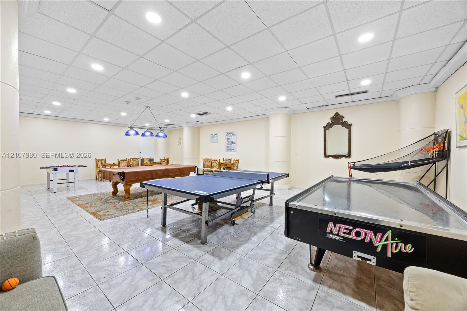 Spacious room featuring neutral wall tones, large-format tile flooring, recessed ceiling lighting, and a drop ceiling grid