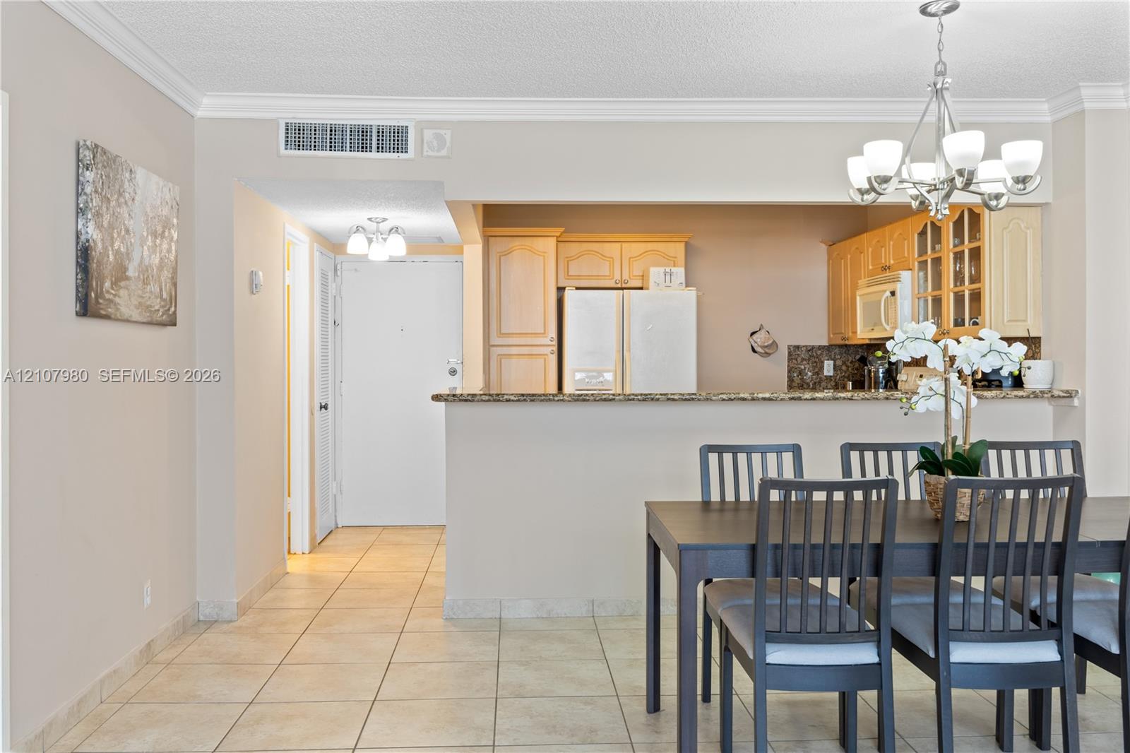 Kitchen featuring wood cabinetry, stone countertops, and a breakfast bar, complemented by tile flooring and a multi-light chandelier