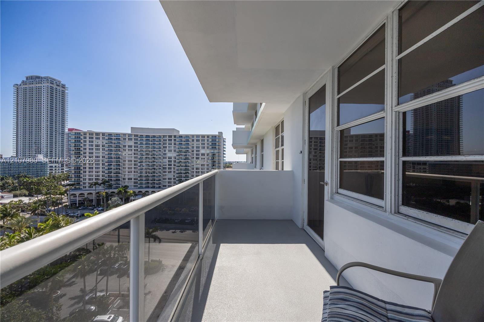 Private covered balcony featuring a glass and metal railing, concrete flooring, and large windowed exterior wall