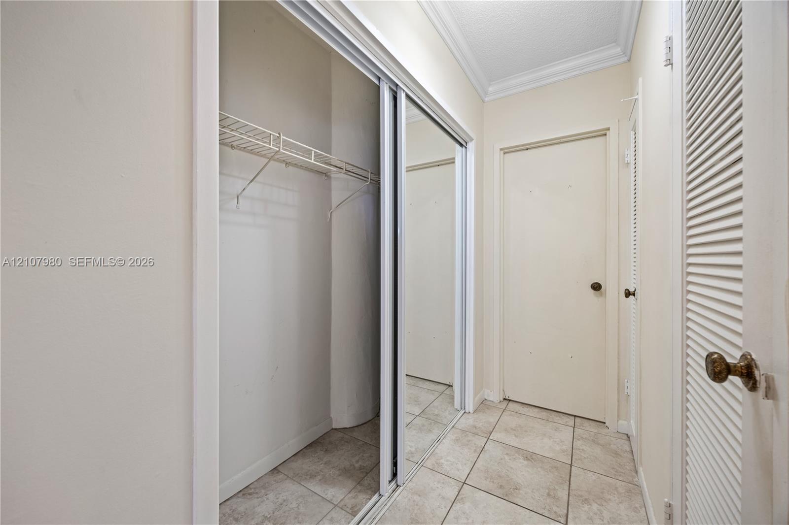 Closet featuring mirrored sliding doors, integrated wire shelving, crown molding, and tiled flooring