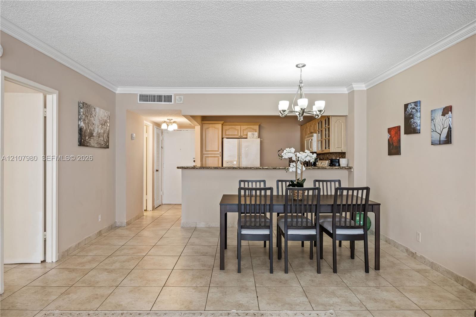 Ceramic tile flooring, crown molding, multi-arm chandelier, and a kitchen peninsula with stone-surface countertop