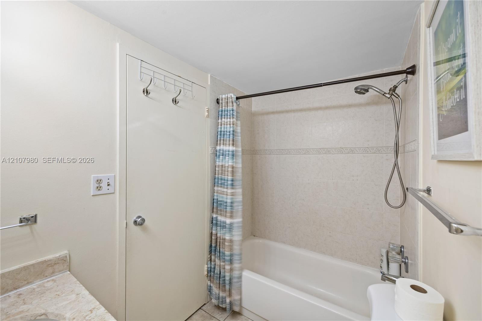 Bathroom featuring a tiled tub surround, a shower system with an adjustable handheld sprayer, and a stone-surface vanity countertop