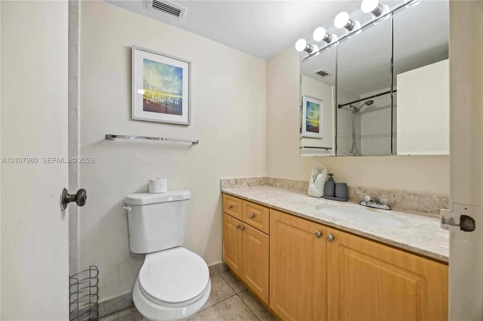 Full vanity with stone-finish countertop, integrated sink, three-door mirrored medicine cabinet, and wood-finish cabinetry