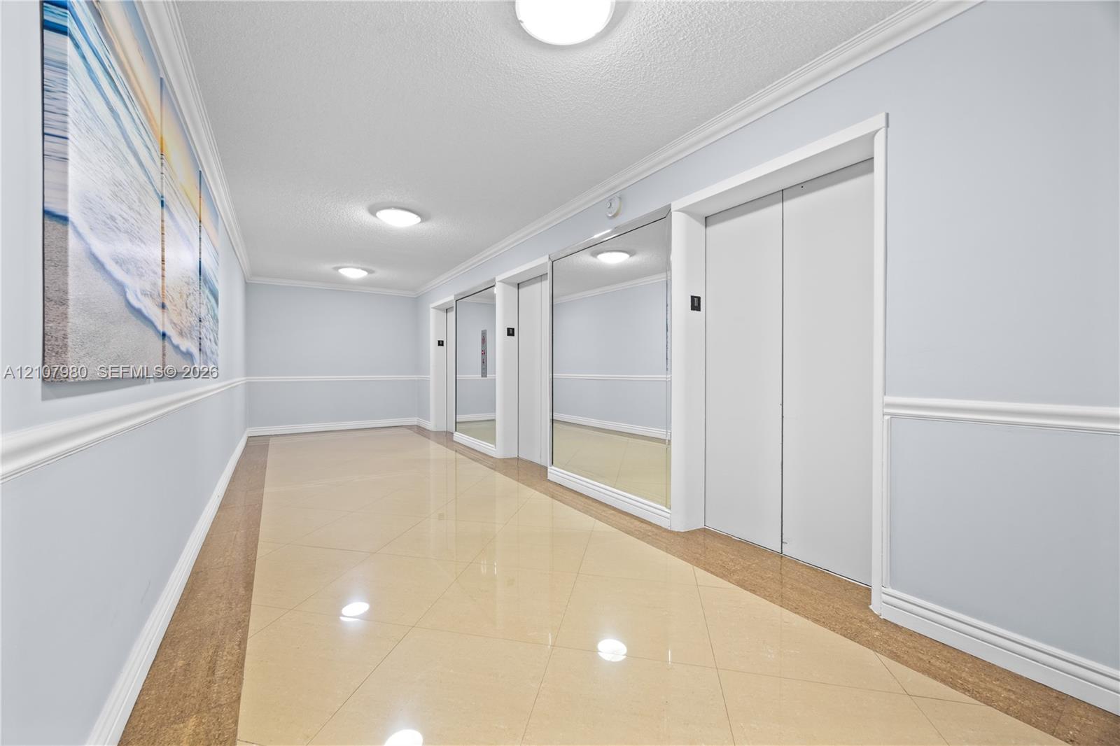 Common hallway featuring polished tile flooring, wall-mounted mirrors, crown molding, chair rail trim, and flush-mount ceiling lighting