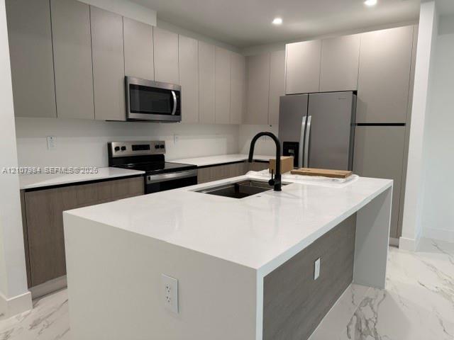 Kitchen featuring flat-panel cabinetry, a central island with a stone-finish countertop, stainless steel appliances, a matte black faucet, and large-format tile flooring