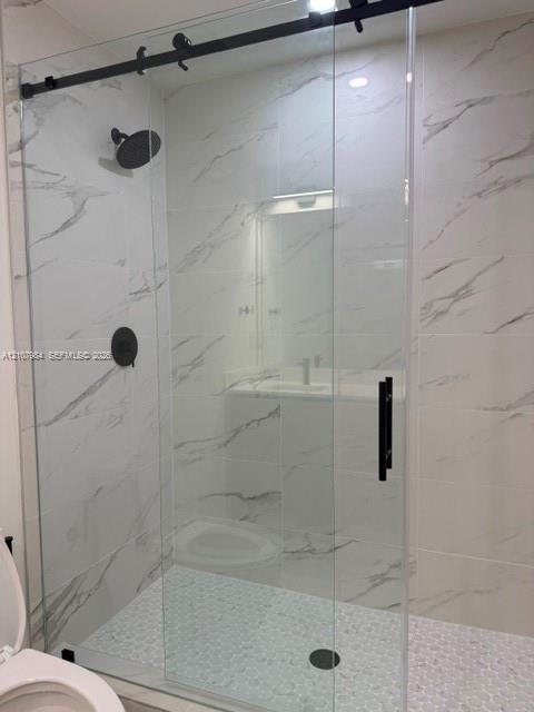Walk-in shower featuring large-format stone-pattern tile, a glass sliding door with matte black hardware, a round rainfall showerhead, and a textured pebble tile floor Walk-in shower featuring large-format stone-pattern tile, a glass sliding door with matte black hardware, a round rainfall showerhead, and a textured pebble tile floor
