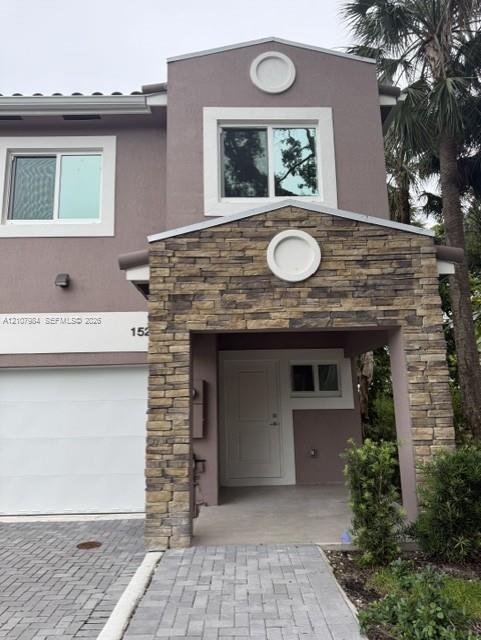 Multi-level exterior featuring a stone-veneer entryway, solid panel front door, herringbone-pattern paver driveway, and circular architectural accents