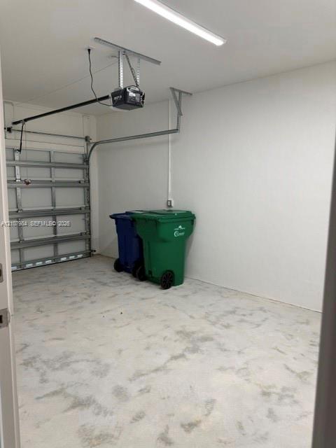 Garage featuring a concrete floor, finished interior walls, an automated door opener, and overhead LED lighting