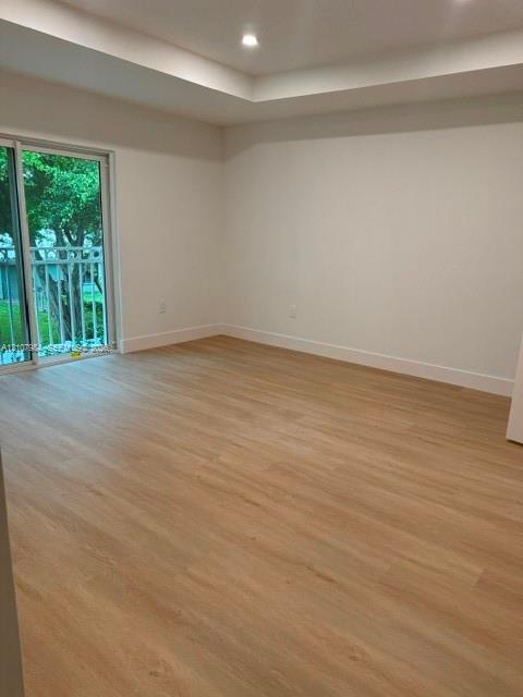 Interior room featuring wood-finish flooring, a tray ceiling, recessed lighting, and a sliding glass door with exterior balcony railing