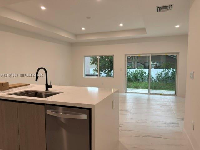 Kitchen island with stone-finish countertop, undermount sink, matte black faucet, and stainless steel dishwasher, featuring large-format tile flooring and recessed lighting