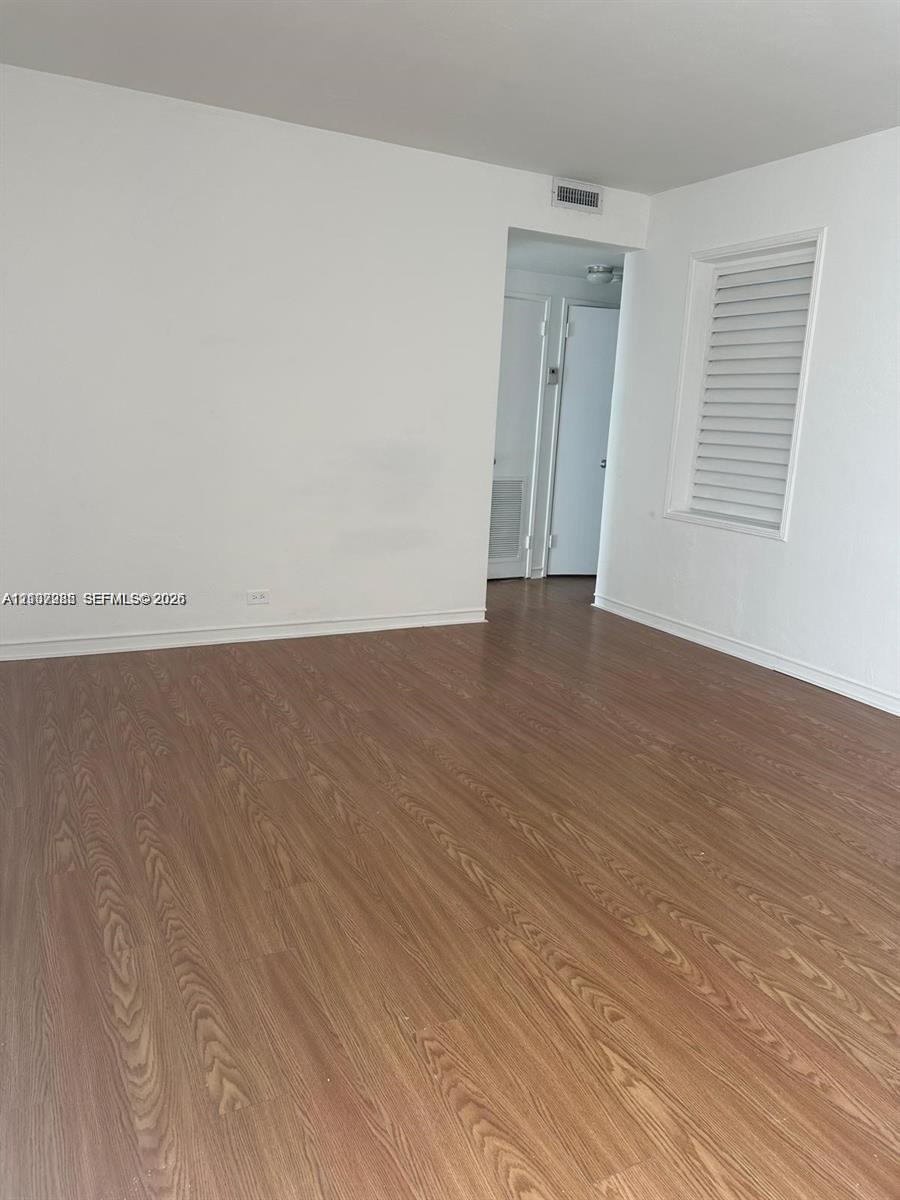 Wood-finish flooring, neutral walls, and a window with a fitted shutter