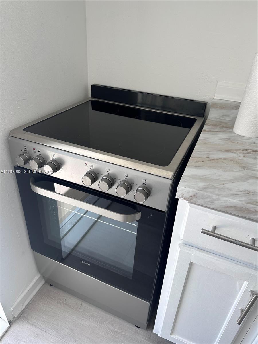 Stainless steel electric range with glass cooktop, paired with white shaker-style cabinetry and neutral stone-finish countertop