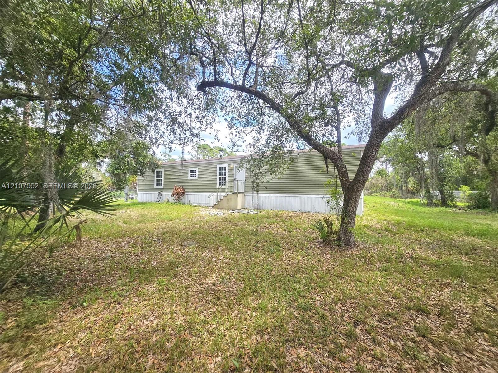 Exterior featuring olive-toned horizontal siding, white trim, multiple windows, and a grassy lot with mature trees