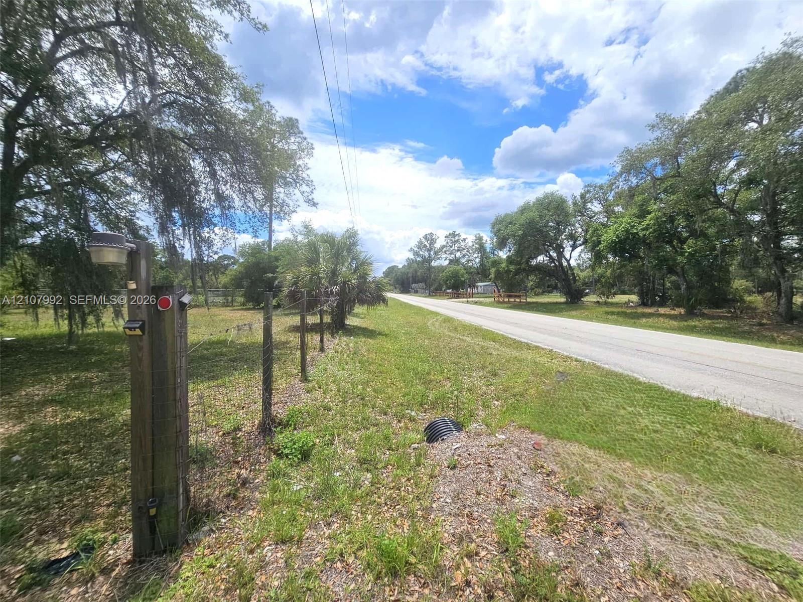 Expansive open lot featuring mature oak trees, wire perimeter fencing, and established ground cover