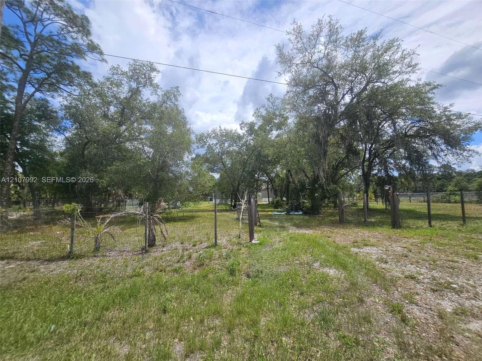 Expansive lot featuring mature trees, partial wire fencing, and cleared terrain