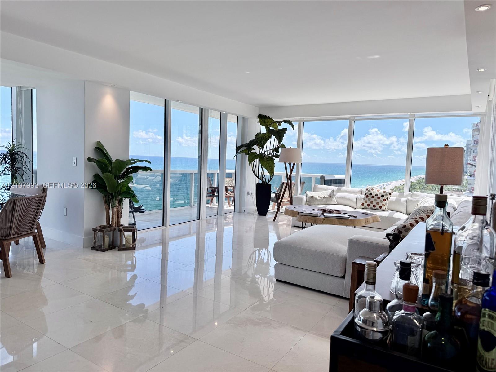 Open-concept interior featuring floor-to-ceiling glass paneling, polished stone-finish tile flooring, recessed ceiling lighting, and a private balcony