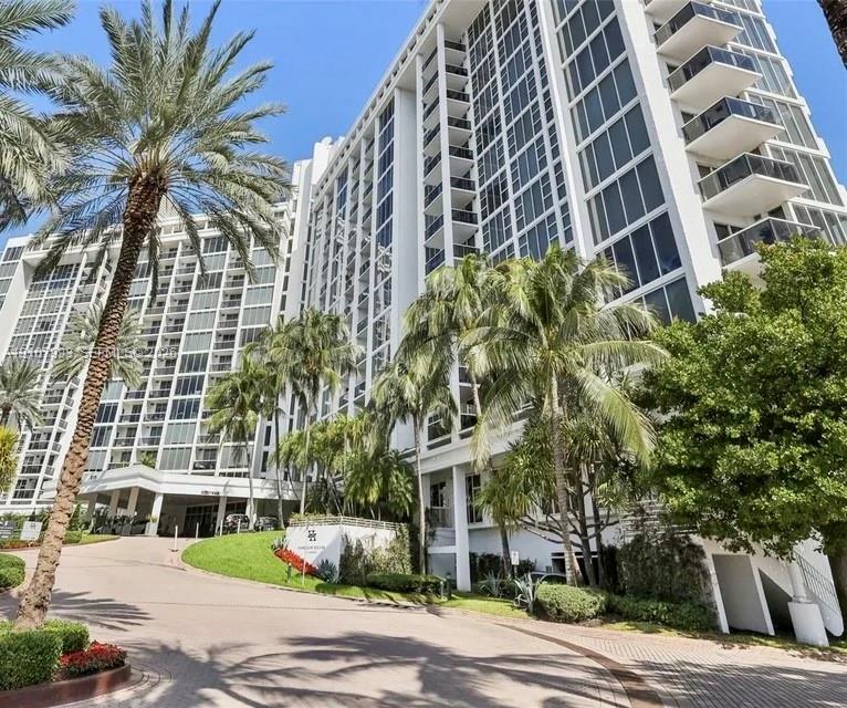 High-rise architectural exterior featuring glass curtain walls, private balconies, a porte-cochre entry, and mature landscaping