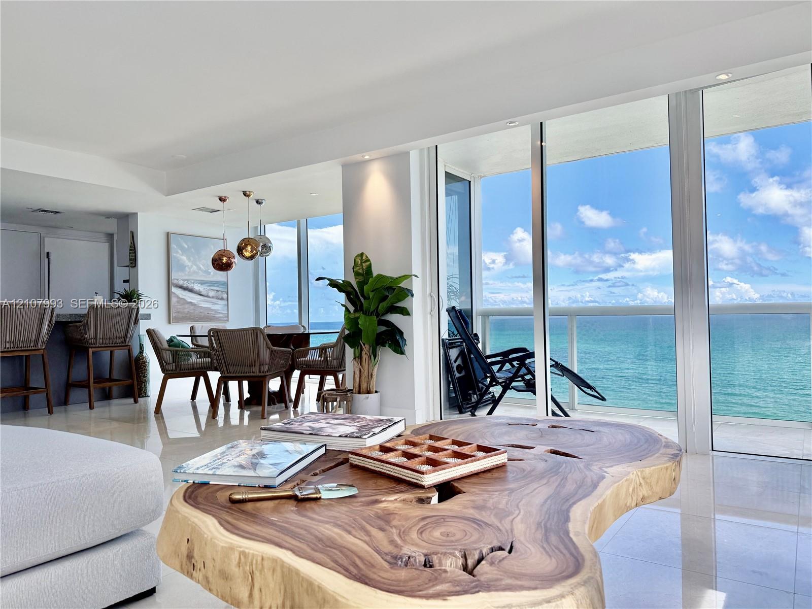 Floor-to-ceiling glass panel walls, polished tile flooring, recessed ceiling lighting, built-in kitchen cabinetry, and an attached balcony overlooking the ocean