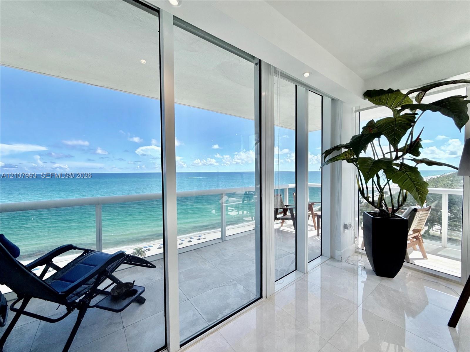 Floor-to-ceiling glass sliding doors, large-format tile flooring, and a glass-paneled balcony overlooking the ocean