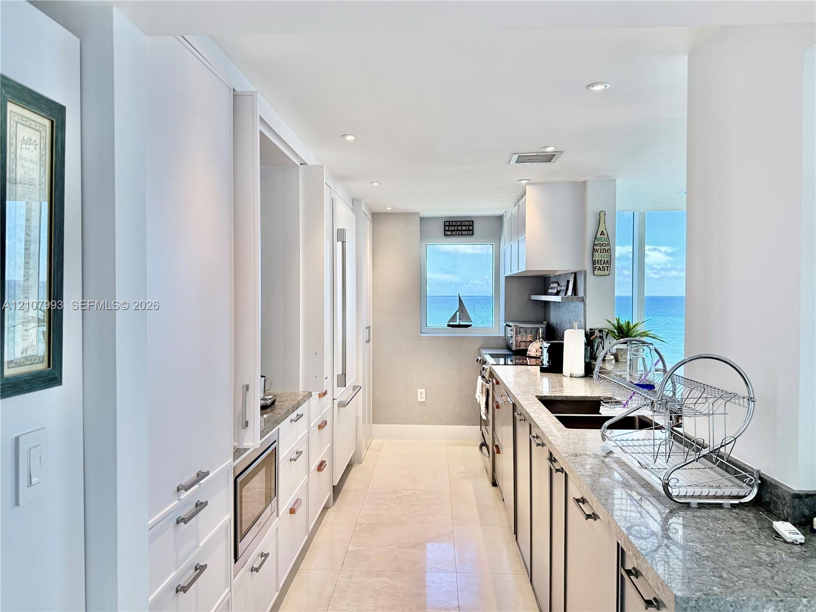 Kitchen featuring flat-panel white cabinetry, stone-surface countertops, recessed lighting, and large windows with ocean scenery