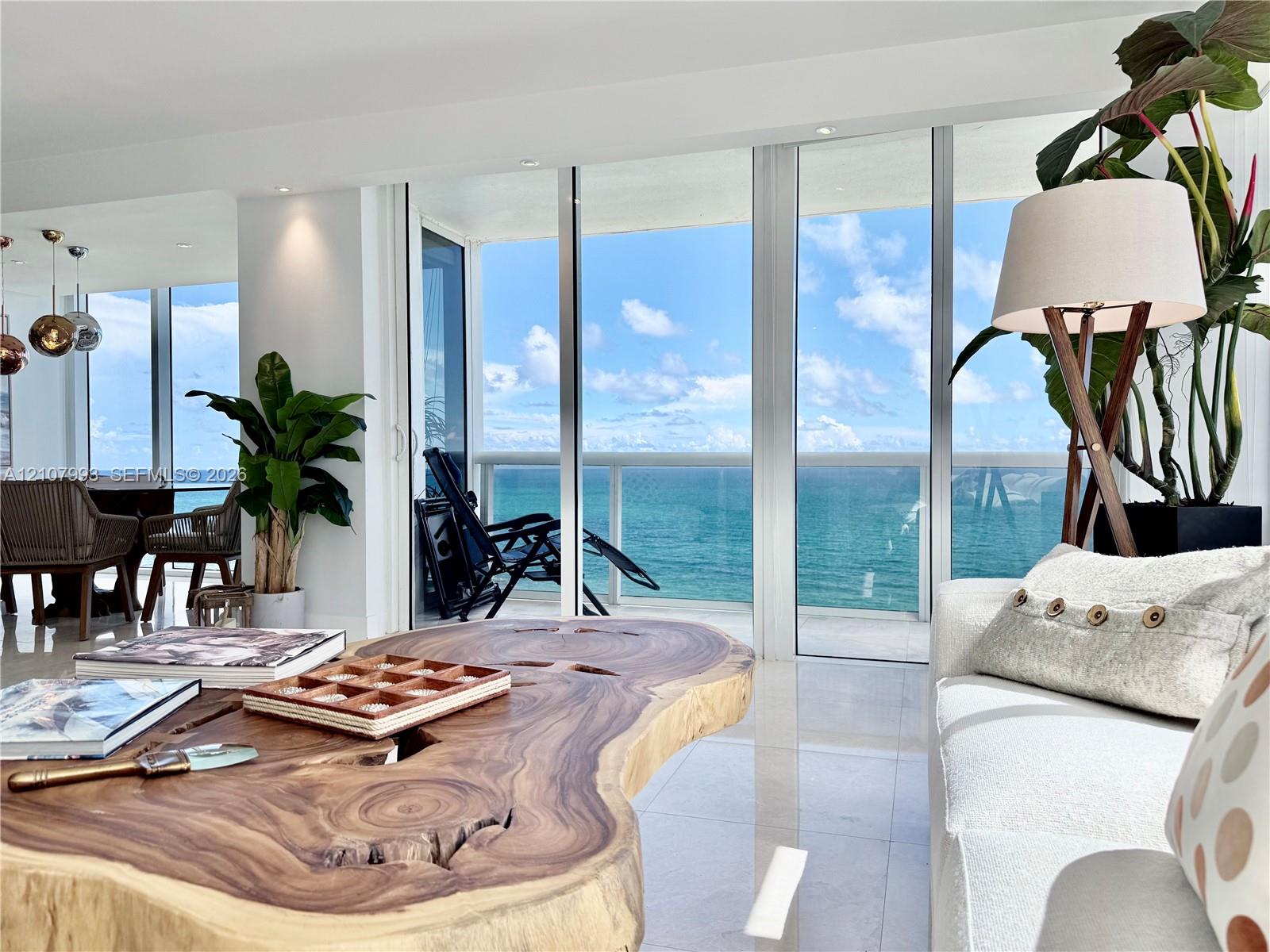 Floor-to-ceiling glass panel walls, light-reflective stone flooring, recessed ceiling lighting, and a glass-railed balcony overlooking the ocean