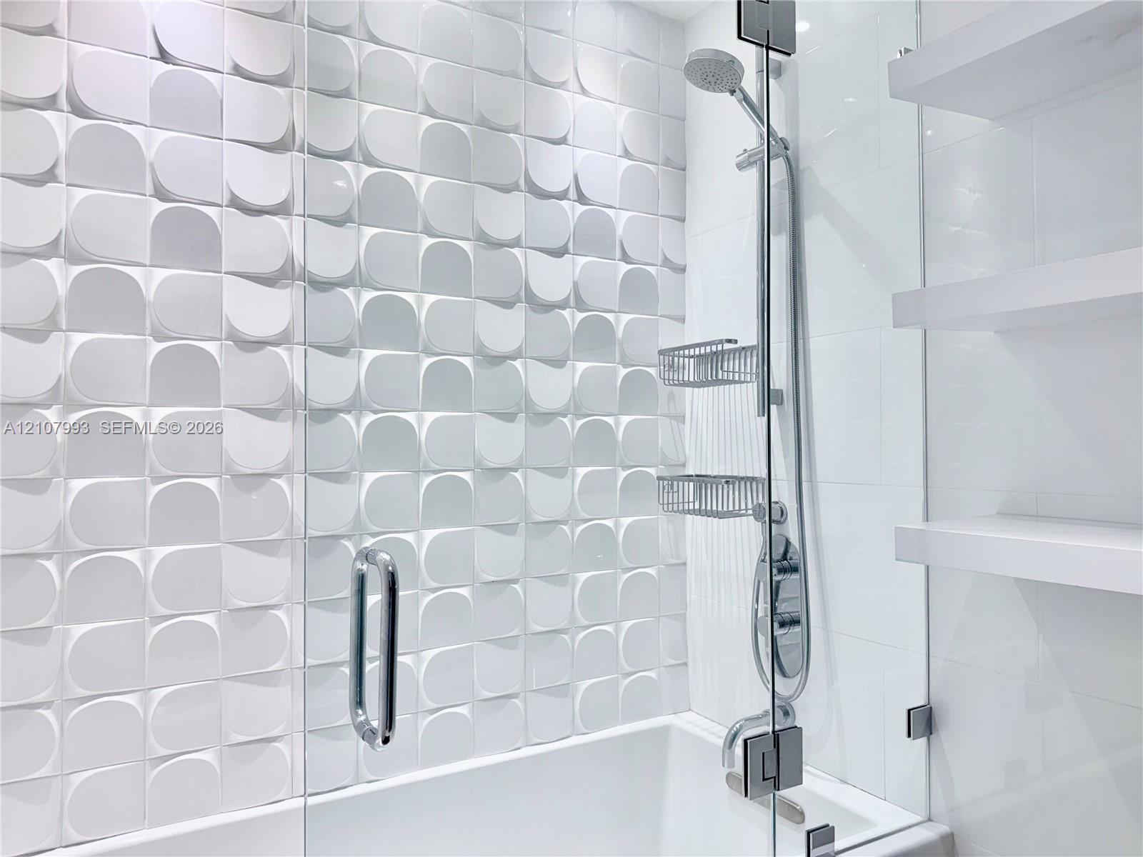 Textured three-dimensional wall tile, glass-enclosed shower, adjustable height handheld shower head, and built-in floating shelves