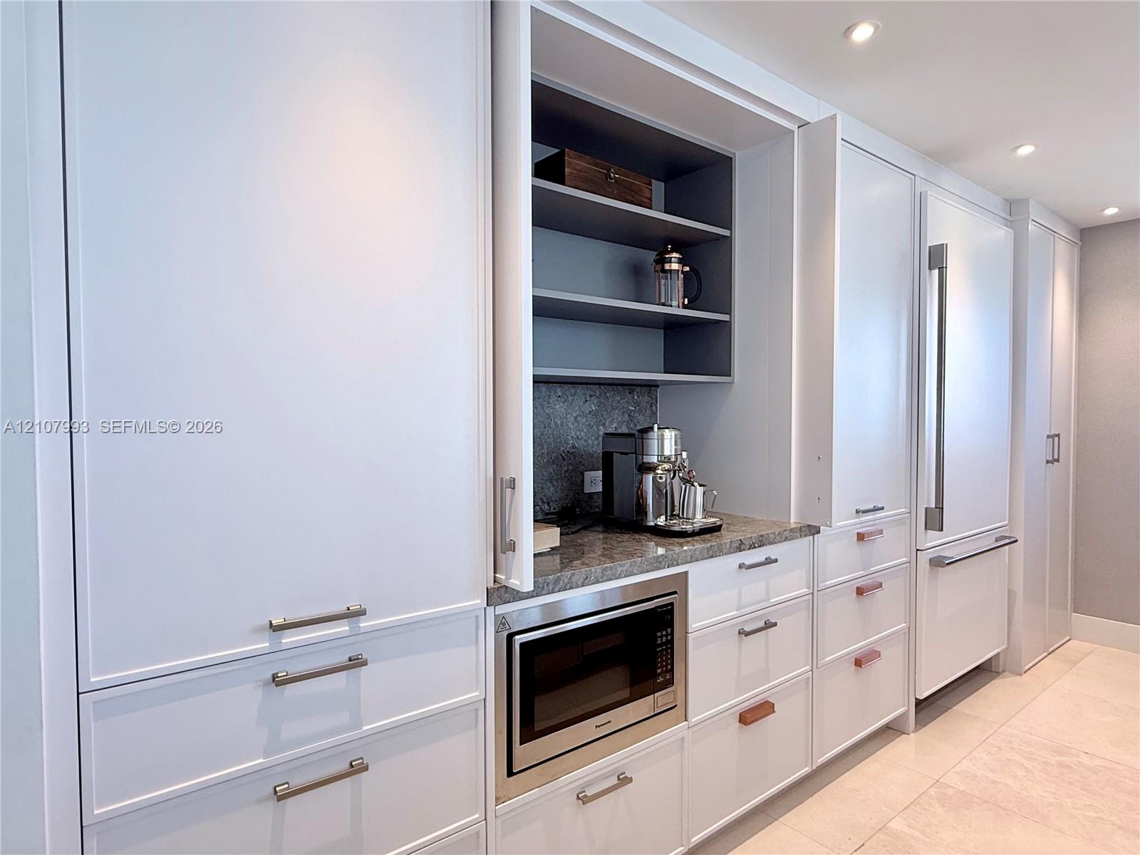 Floor-to-ceiling cabinetry with custom millwork, integrated refrigerator, stone countertop, built-in microwave, and recessed lighting