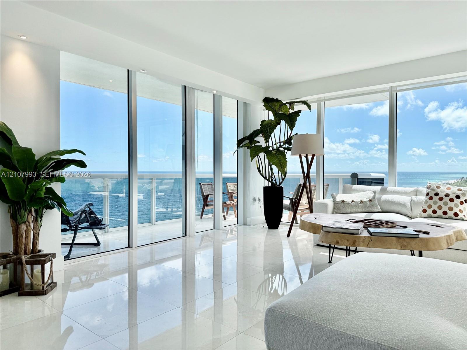 Floor-to-ceiling glass walls, polished stone flooring, recessed lighting, and a glass-railed balcony overlooking the ocean