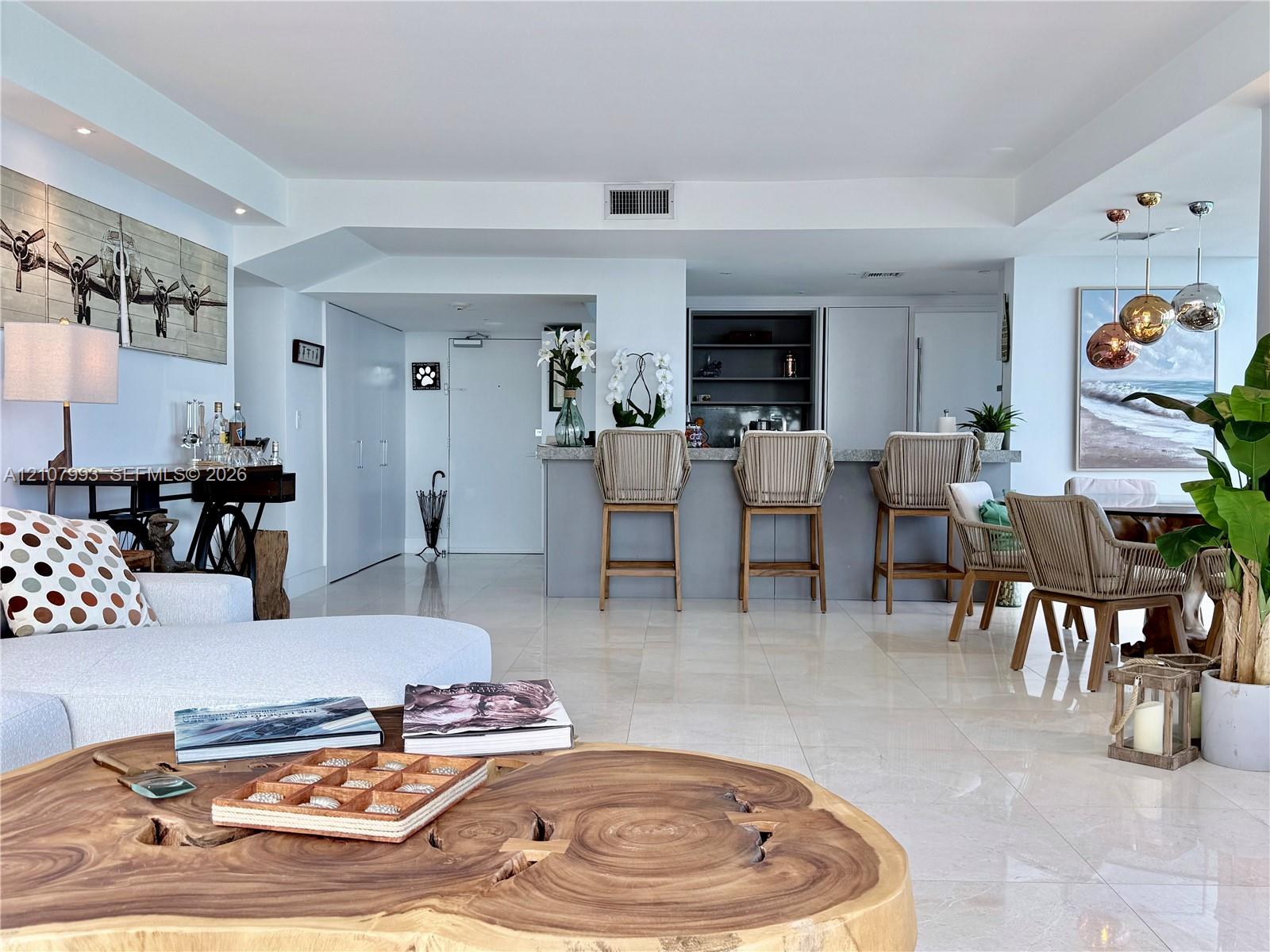 Open-concept living area featuring large-format tile flooring, a built-in kitchen bar with stone countertop, recessed lighting, and sleek custom cabinetry