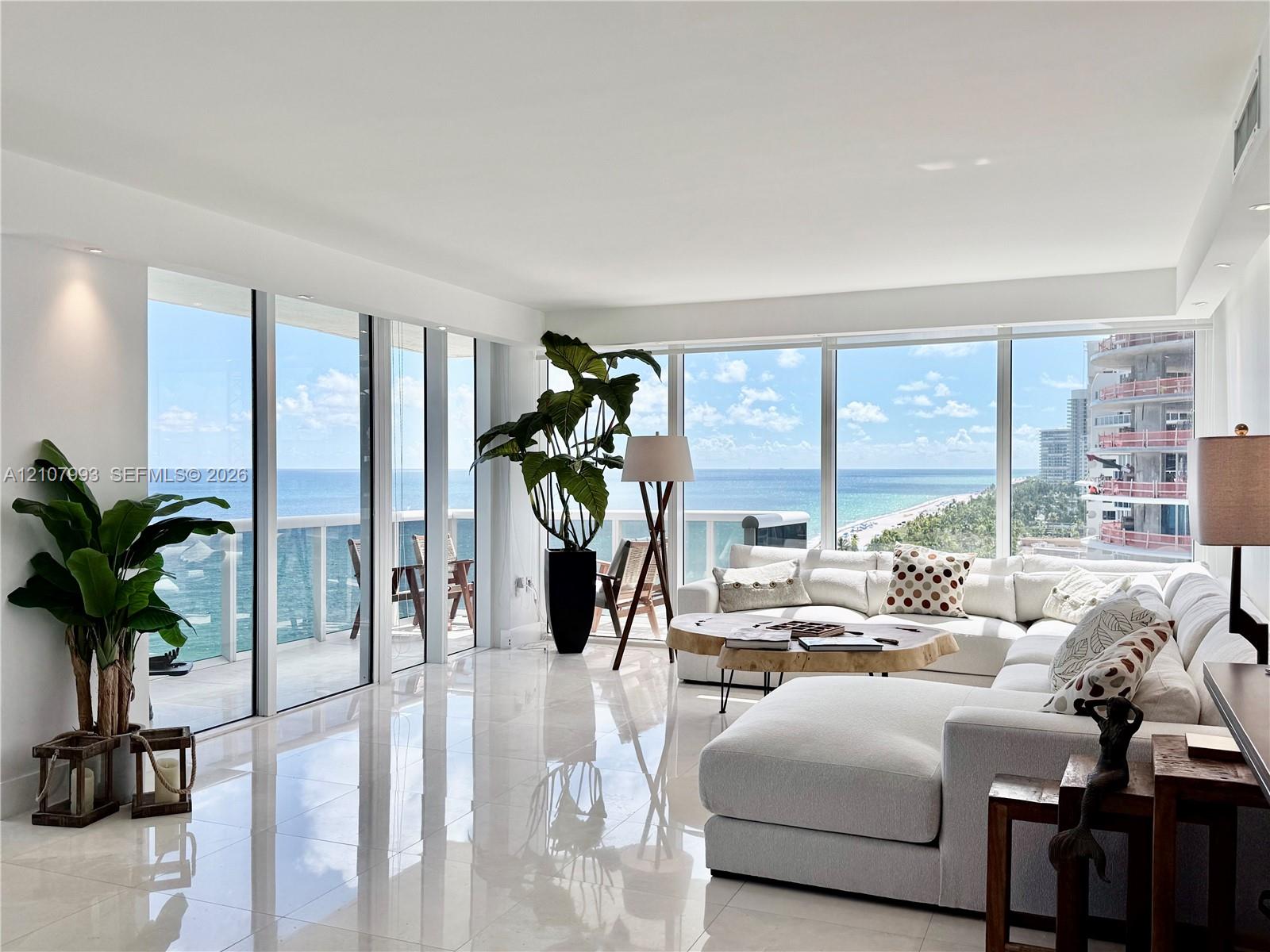 Floor-to-ceiling windows, white polished tile flooring, recessed lighting, and a glass-railed balcony with ocean and coastline exposure