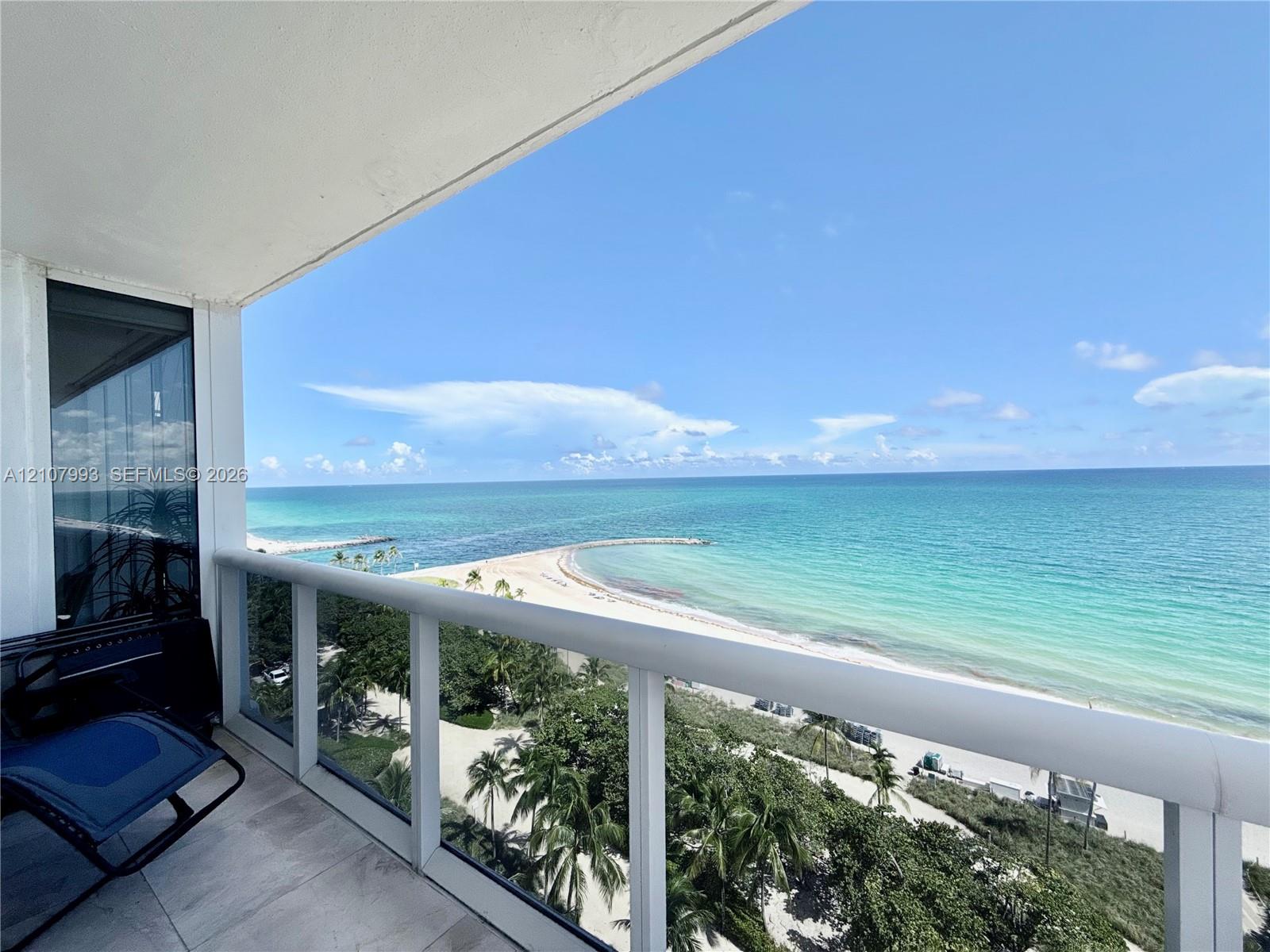 Covered balcony featuring glass-panel railings, tile flooring, and direct oceanfront scenery