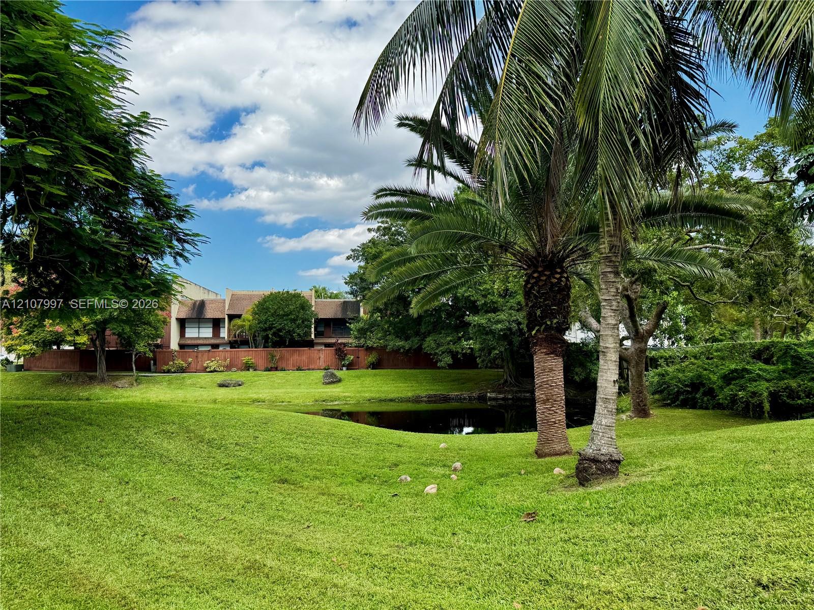 Expansive grounds featuring a manicured lawn, mature palm trees, and a pond
