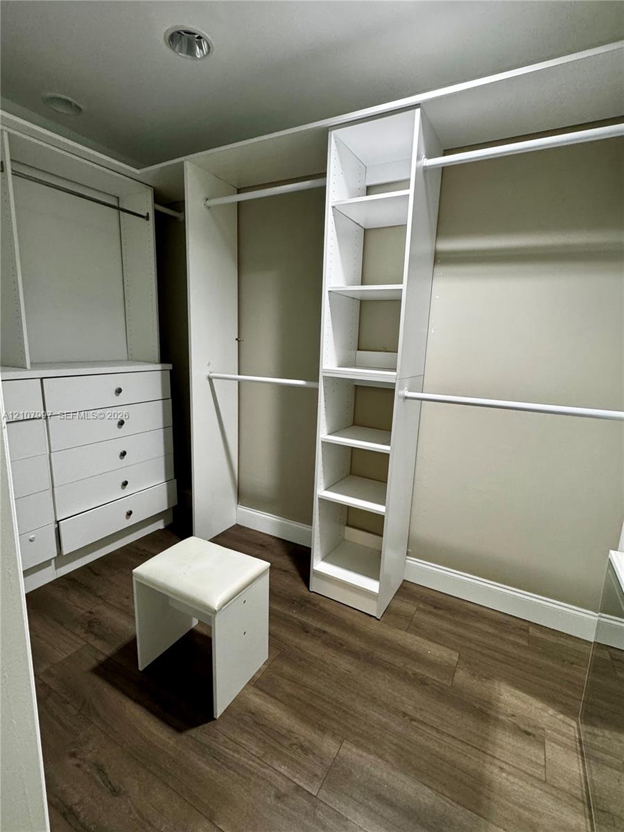 Walk-in closet featuring white built-in shelving, integrated dresser drawers, hanging rods, and wood-finish flooring