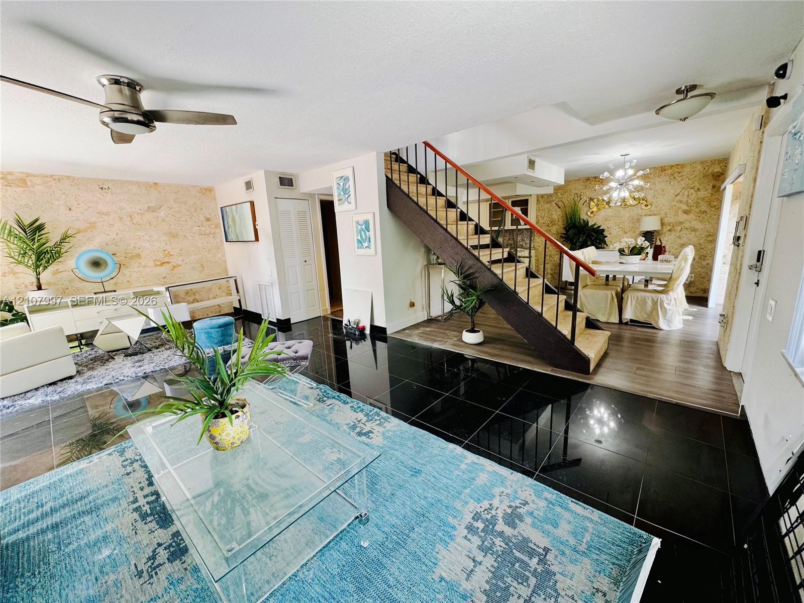 Professional pictures coming soon! Open-concept interior featuring textured stone accent walls, high-gloss black tile flooring, and a staircase with wood beam & metal handrail