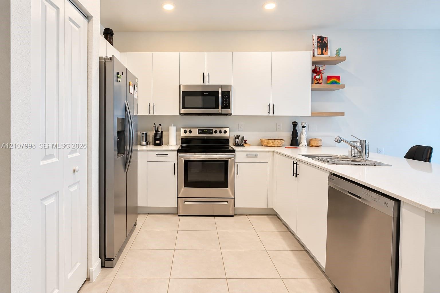 Kitchen featuring white flat-panel cabinetry, stainless steel appliances, white solid-surface countertops, tile flooring, and built-in floating wood shelving