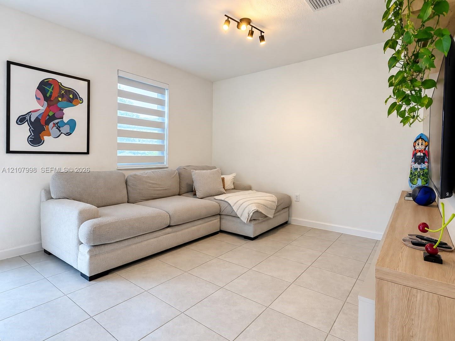 Neutral-toned ceramic floor tiling, adjustable dual-shade window treatments, and multi-directional track lighting