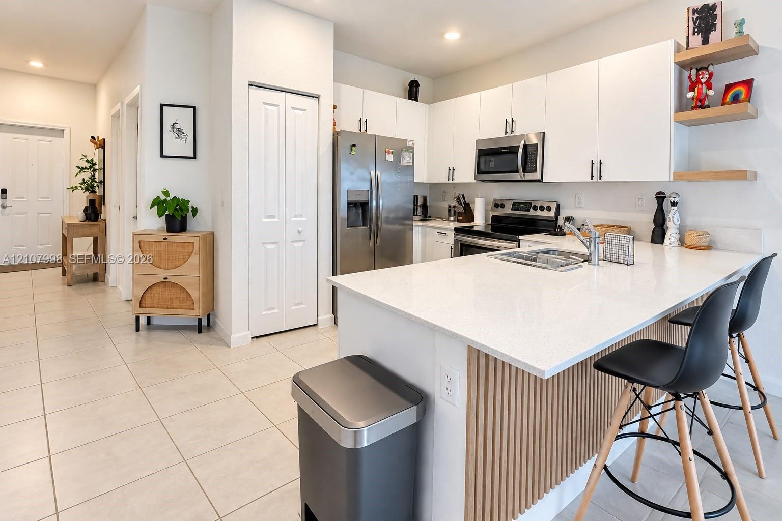 Kitchen featuring white flat-panel cabinetry, a stone-finish island countertop, vertical wood-slat island detailing, stainless steel appliances, and floating shelves