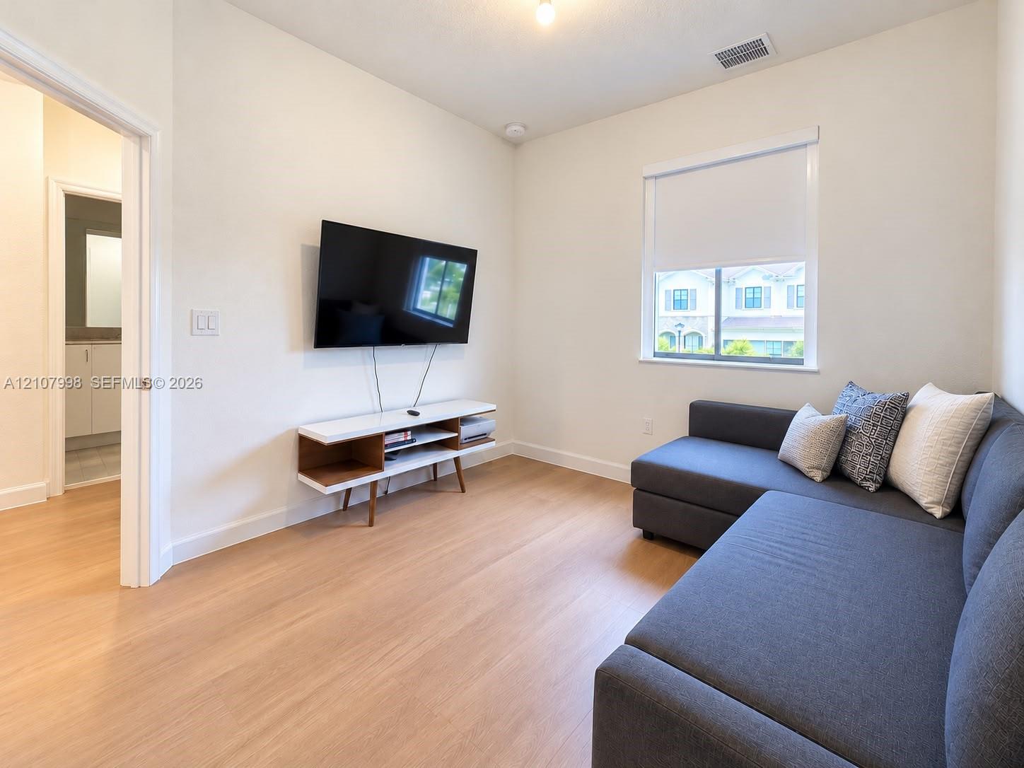 Neutral interior featuring wood-finish flooring, crisp white walls, and a single-hung window with a roller shade
